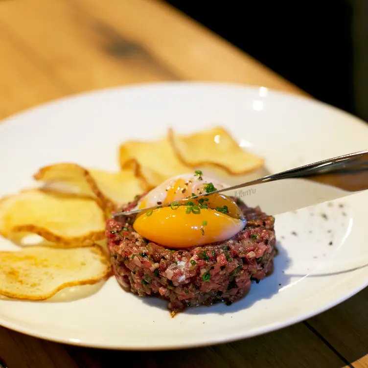 A diner cuts into the egg yolk on top of a steak tartare dish served at Le Petit Flot, one of the best French restaurants in Sydney.