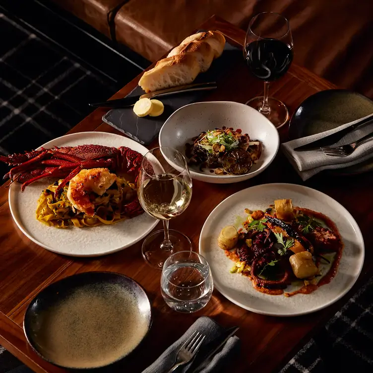 Several dishes with seafood, pasta and bread served alongside wine at Coal Cellar + Grill.