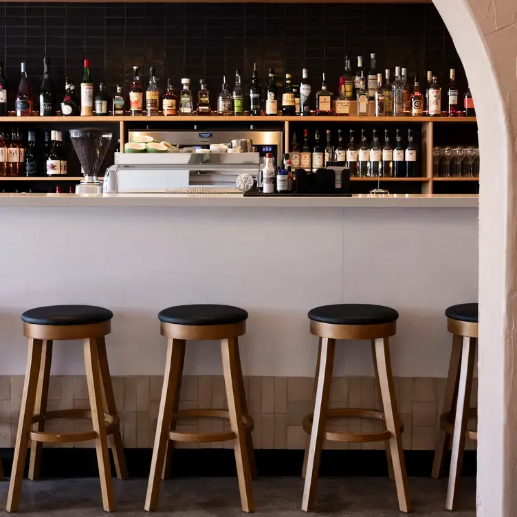 The bar at Four Sides Bar and Kitchen, with stools lined up in front of the bar and rows of wines and spirits behind it.