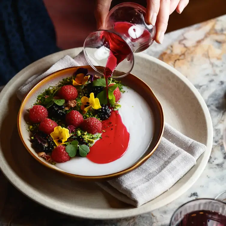 A waiter pours a red sauce over a dessert of berries and flower garnishes at Babylon RESTAURANT, one of the best dinner date restaurants in Sydney.