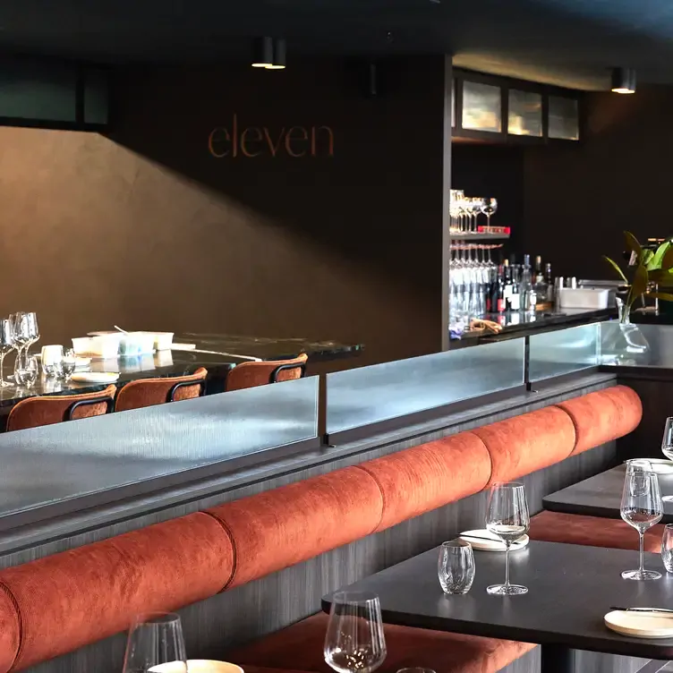 The interior of eleven Restaurant & Piazza, showing several tables with red and grey booth seating and a bar in the background.