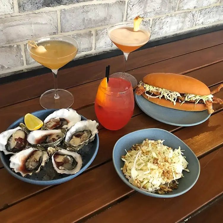 A few dishes, including a crab roll and a plate of mussels, and three colourful cocktails served at King Crab Co.