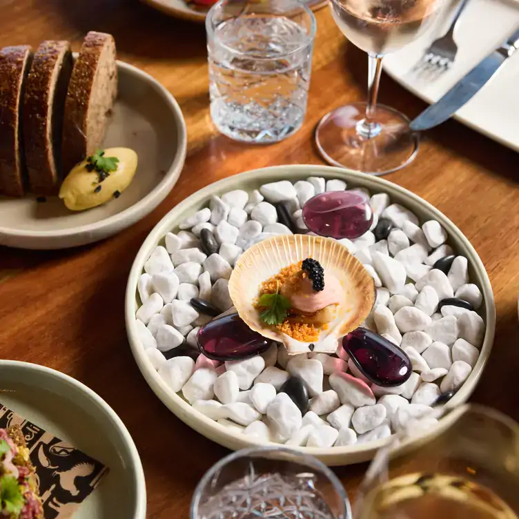 A seafood starter served in a clamshell alongside drinks and bread at Squire’s Waterfront Restaurant, one of the most romantic restaurants in Sydney.