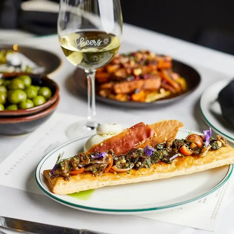 A thin, rectangular pastry topped with vegetables and cured meat served alongside other dishes and a glass of white wine at Ripponlea Food & Wine, one of the best new restaurants in Melbourne in 2024.