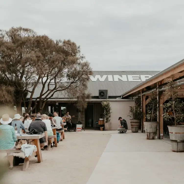 The outdoor seating area of Phillip Island Winery, one of the best wineries in Victoria. In front of the tables, someone is playing guitar.