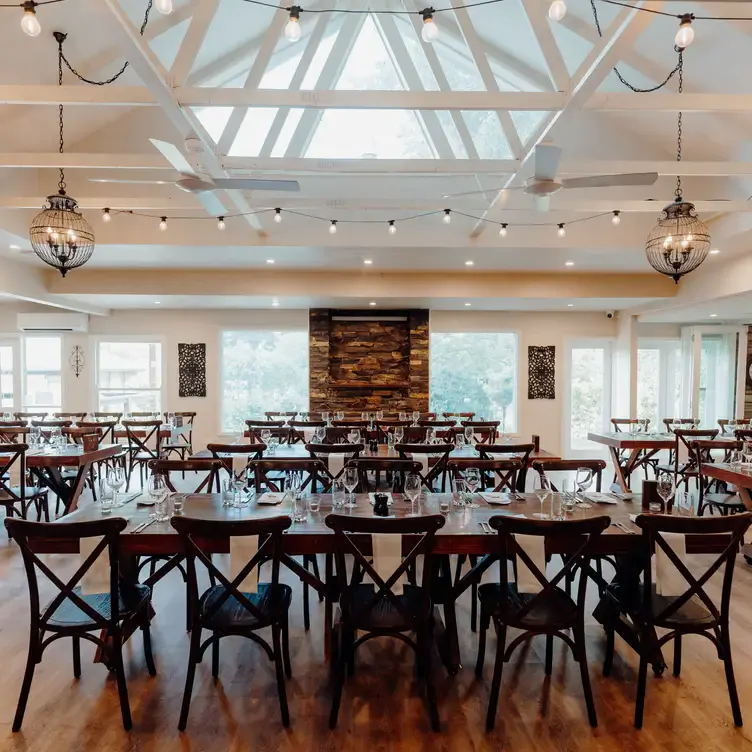 The interior of Immerse Yarra Valley, which hosts one of the best winery lunches in Victoria. It has white-painted walls and ceiling with exposed beams, a brickwork fireplace and wooden tables and chairs.