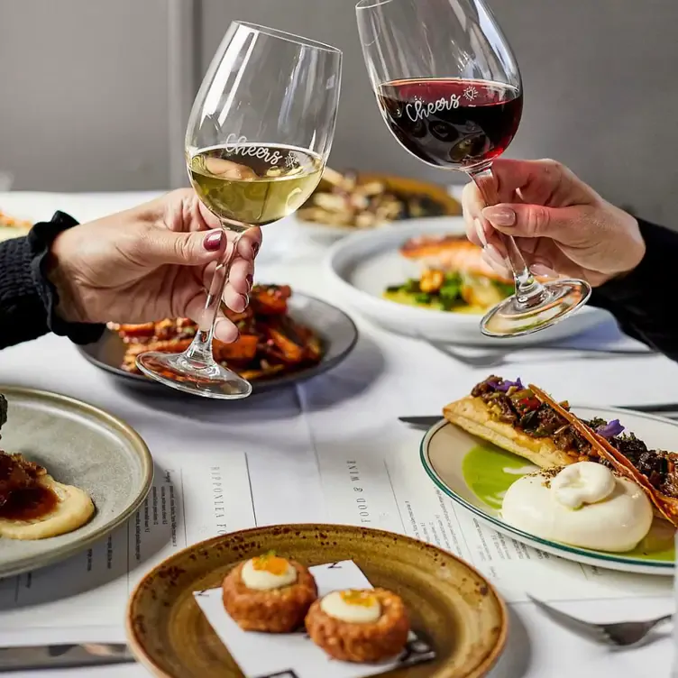 Two diners clink glasses of red and white wine over a table packed with dishes at Ripponlea Food & Wine, one of the best new restaurants in Melbourne.