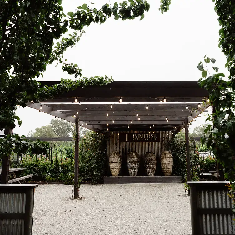 An outdoor area at Immerse Yarra Valley with bench seating and a large shelter strung with hanging lights.