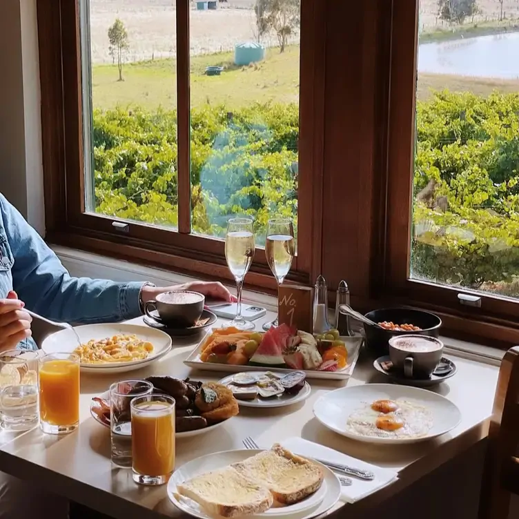 A table laid with breakfast foods including eggs, toast and fruit, served alongside glasses of orange juice, champagne and cappuccinos.