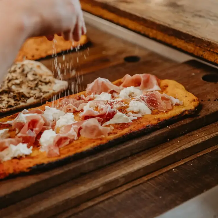 Someone dusts shaved cheese on top of a long pizza topped with cured meat at T’Gallant Vineyard, one of the best winery restaurants in Victoria.