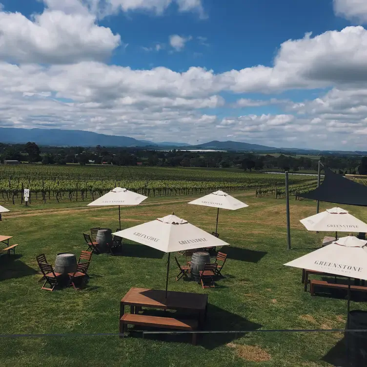 Several tables with bench seating shaded by umbrellas, facing the growing vines of Greenstone Vineyards, one of the best wineries in Victoria.