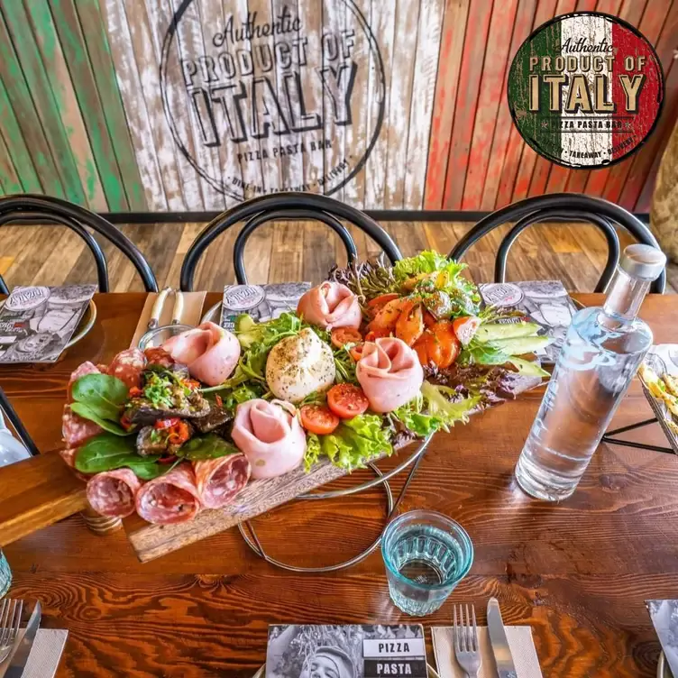 A wooden board topped with carefully arranged salami, ham, tomatoes and leafy greens on a table at Product of Italy Kellyville.