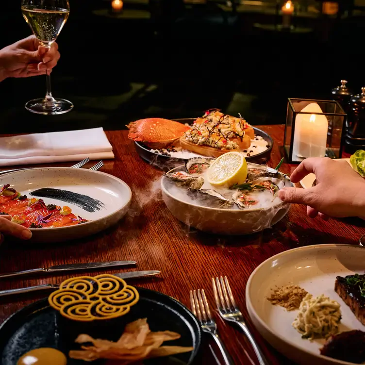 A diner reaches to grab an oyster from a lightly steaming bowl on a table packed with other seafood dishes at Allegro Restaurant.