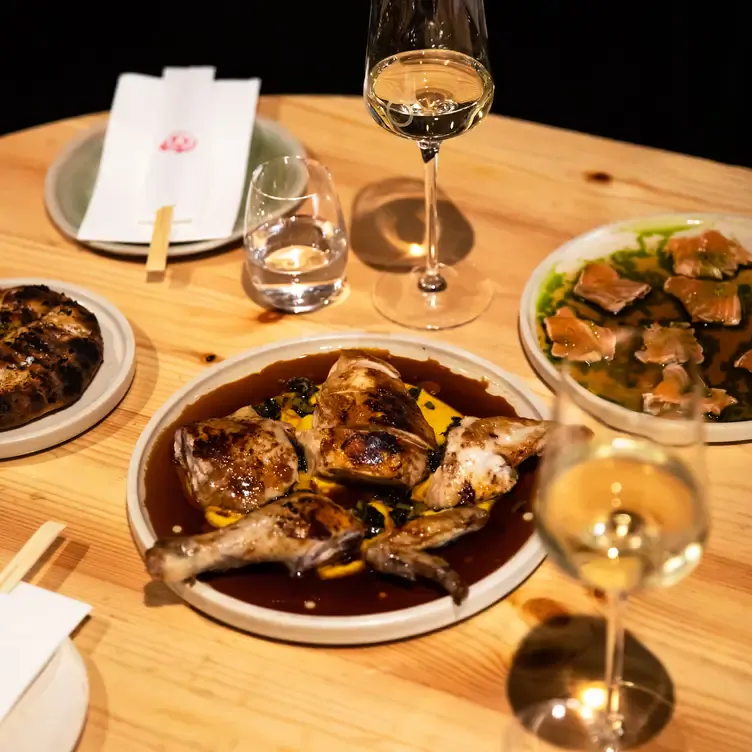 A table at Shobosho laid with a few dishes including chicken drumsticks in a brown sauce alongside glasses of white wine.