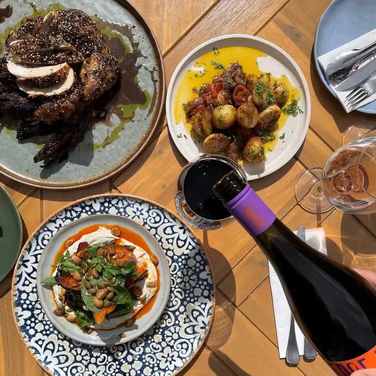 Someone pours wine into a glass surrounded by dishes of meat, potatoes and salad at Lou’s Place, one of the best restaurants in South Australia.