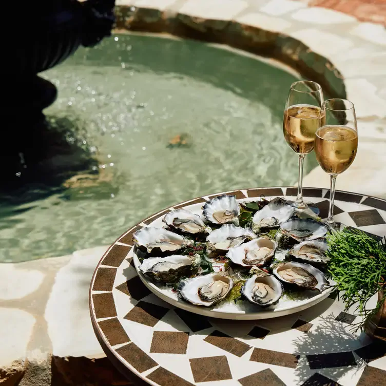 A plate of oysters served alongside glasses of white wine by a fountain at Hardy’s Verandah Restaurant, one of the best regional restaurants in Australia.