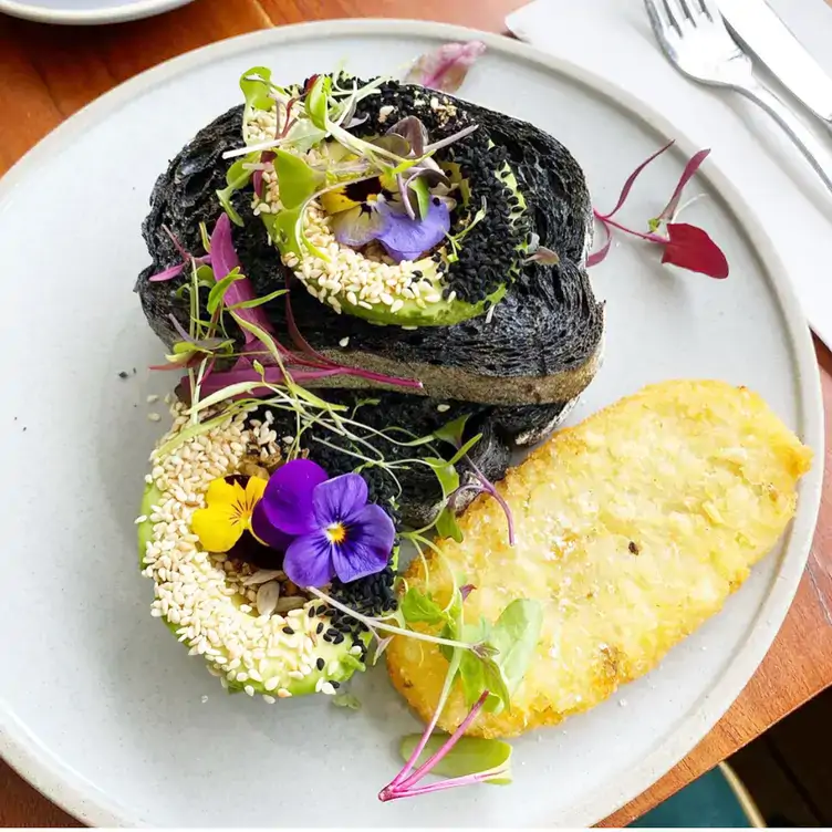 A plate of charcoal toast topped with sliced avocado and served alongside a hash brown at Hello Neighbour Artusi by Night, one of the best brunch places in Adelaide.