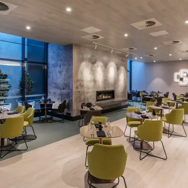 The interior dining space at Restaurant Two14 with green chairs around cream tables, a fireplace and geometric art on the wall.