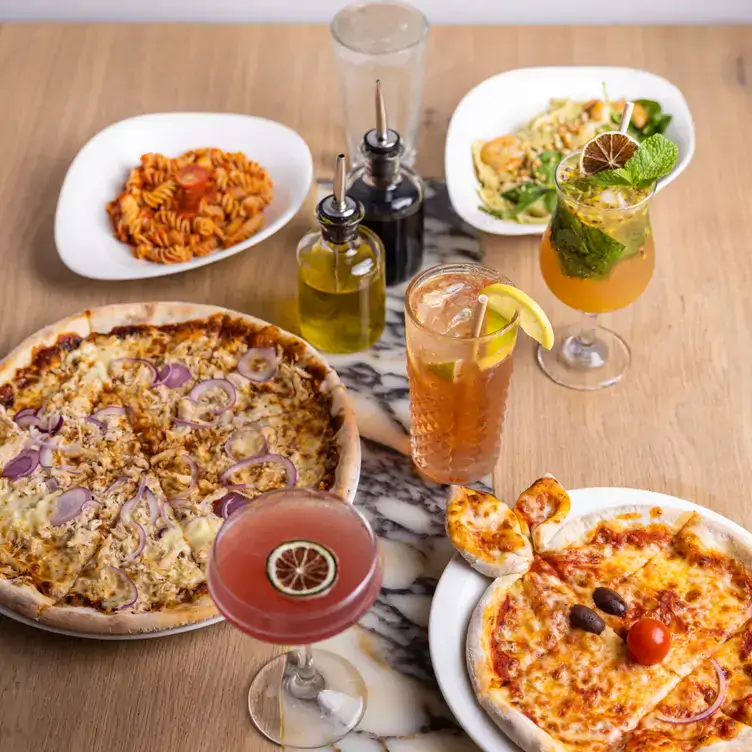 A large and small pizza served alongside two pasta dishes and cocktails at Vapiano - Soul Boardwalk, one of the best family restaurants on the Gold Coast.