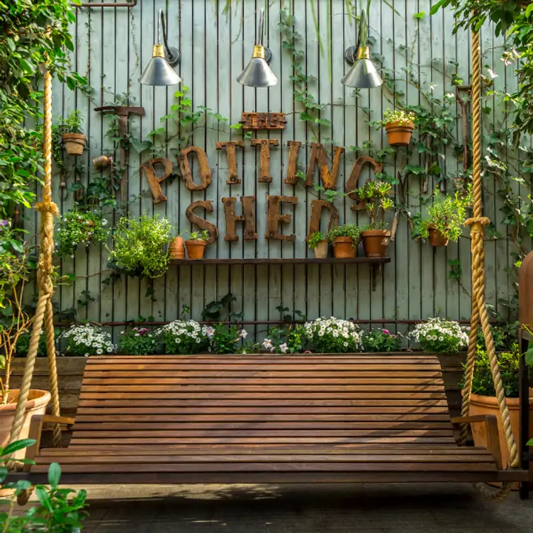 A swing bench backed by flowers and a large sign with the logo of The Potting Shed, one of the best family restaurants in Sydney.