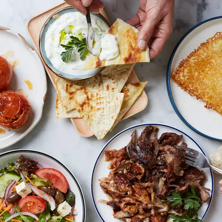 A diner adds tzatziki sauce to some flatbread alongside side meat and salad side dishes at Stalactites Restaurant.