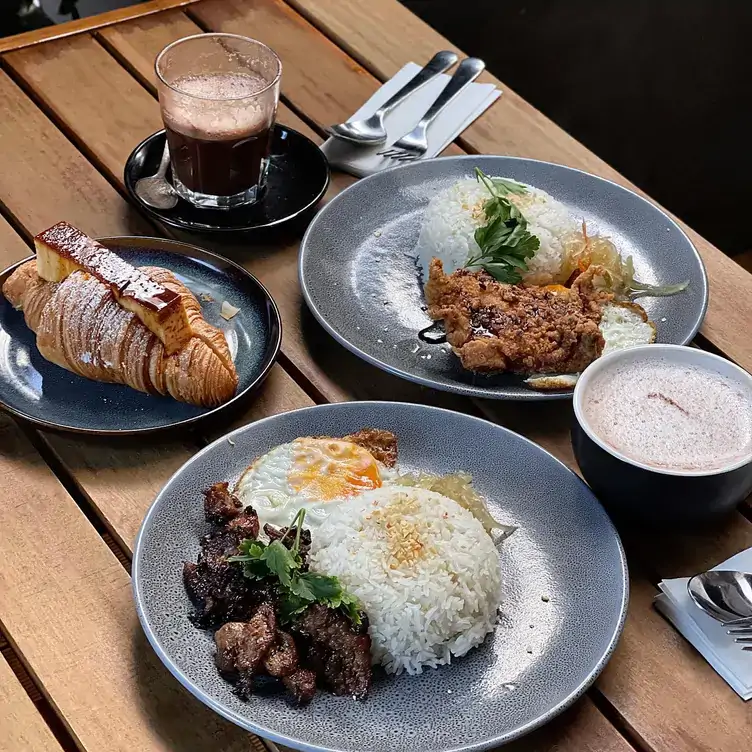 Two dishes of rice, meat and egg served alongside a croissant and two coffees at 34 WYATT STREET, one of the best Adelaide brunch spots.