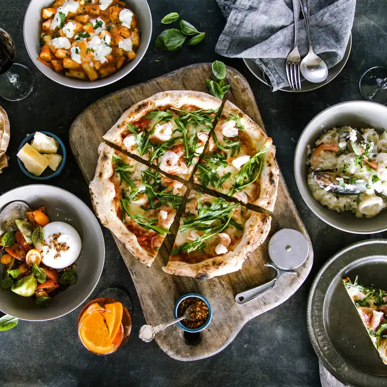 A pizza surrounded by pasta, salad and other dishes at Verace Pizzeria, one of the best family restaurants in Sydney.