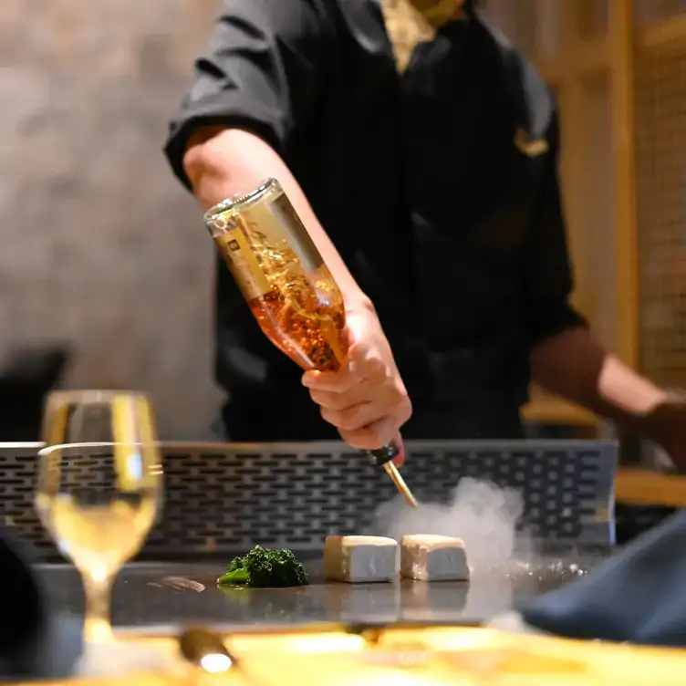 A chef drizzles something onto blocks of tofu at the table at Erato Teppanyaki, one of the best family restaurants in Adelaide.