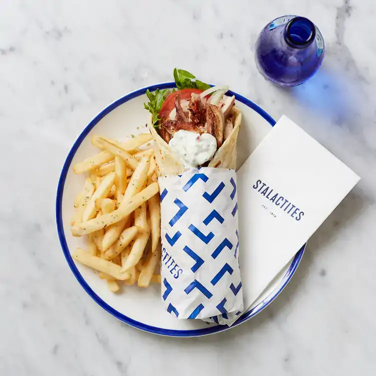 A chicken souvlaki with chips on a plate with a bottle of water at Stalactites Restaurant, one of the best family-friendly restaurants in Melbourne.