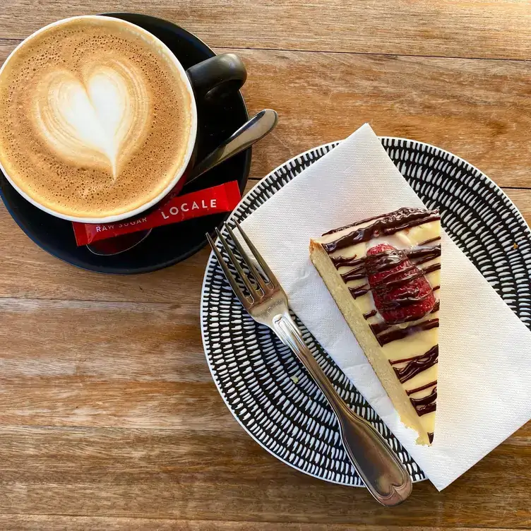 A cappuccino served alongside a cake topped with chocolate and strawberry, served at The Fox’s Hollow, one of the best brunch places in Brisbane.