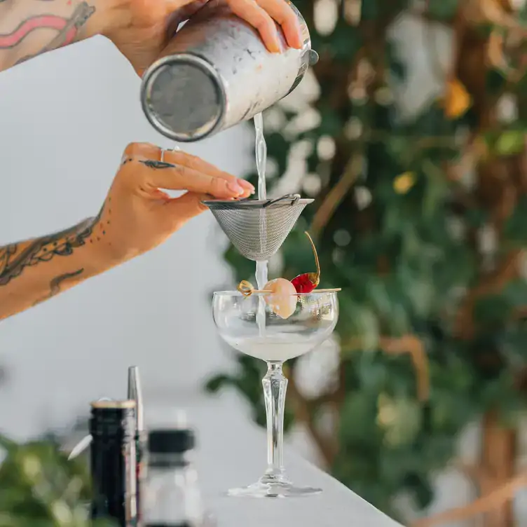 A bartender making a lychee cocktail in a coupe glass at Next Door Burleigh, one of the best restaurants for brunch on the Gold Coast.