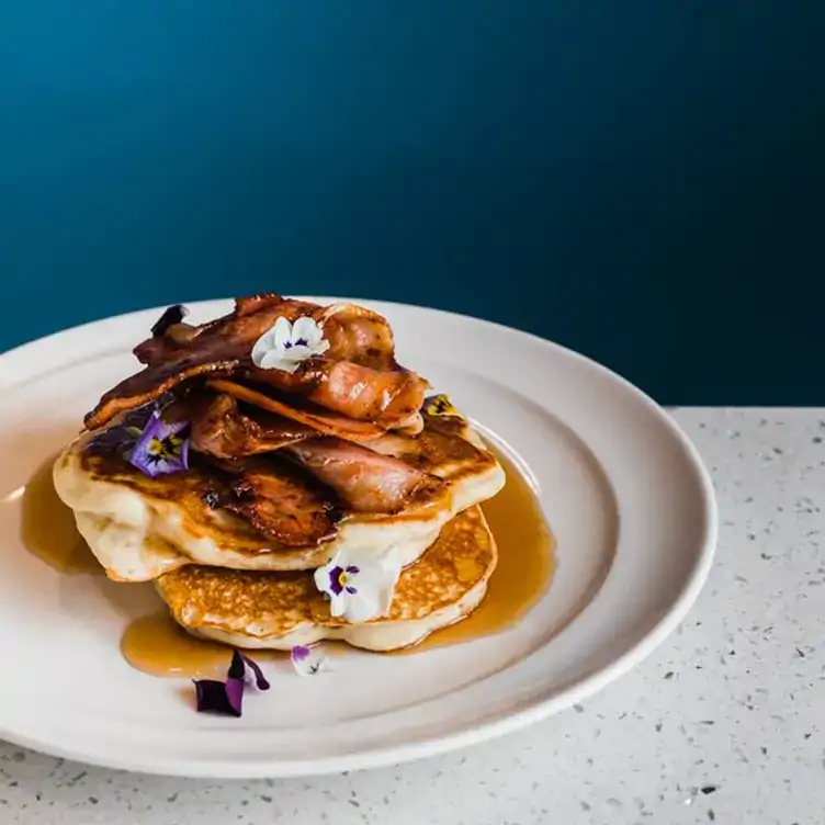 : A stack of pancakes topped with bacon and maple syrup at Big Shots Cafe, one of the best brunch places in Adelaide.