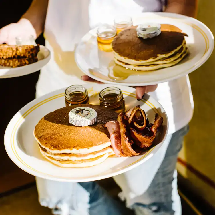 A waiter carries two plates of pancakes with butter, maple syrup and bacon at Happyfield, one of the best family restaurants in Sydney.