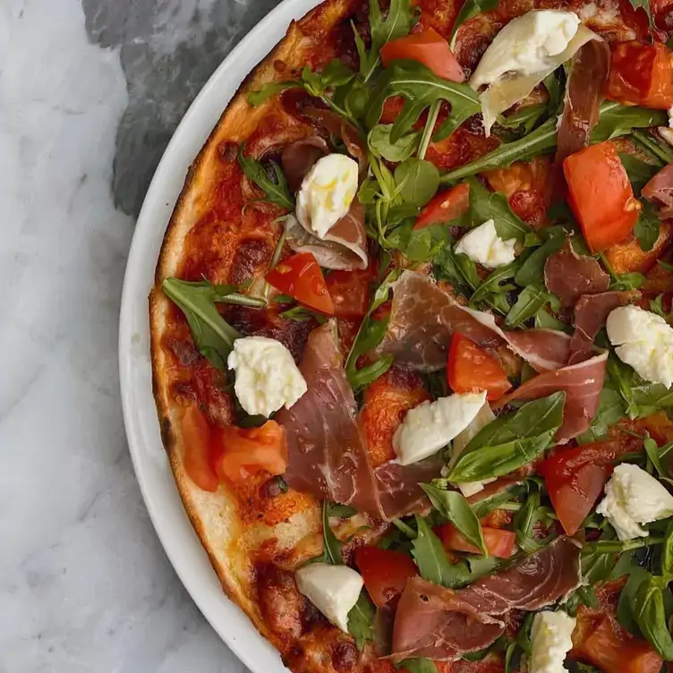 A pizza topped with tomato, rocket and prosciutto served at Balthazar Cafe, one of the best family restaurants in Adelaide.