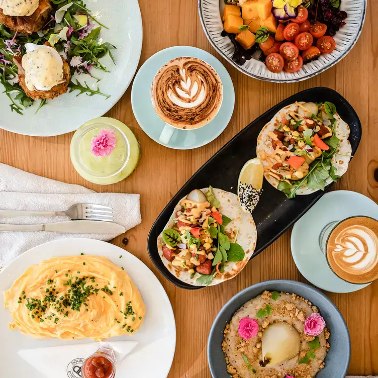 A table laid out with various dishes, including soft tacos and salad, served alongside cappuccinos at Double Barrel Kitchen & Bar.