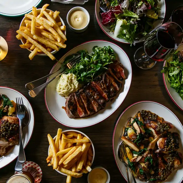 A table laid with multiple dishes including steak, salads and chips at Mount Erica Hotel, one of the best warm and cosy restaurants in Melbourne.