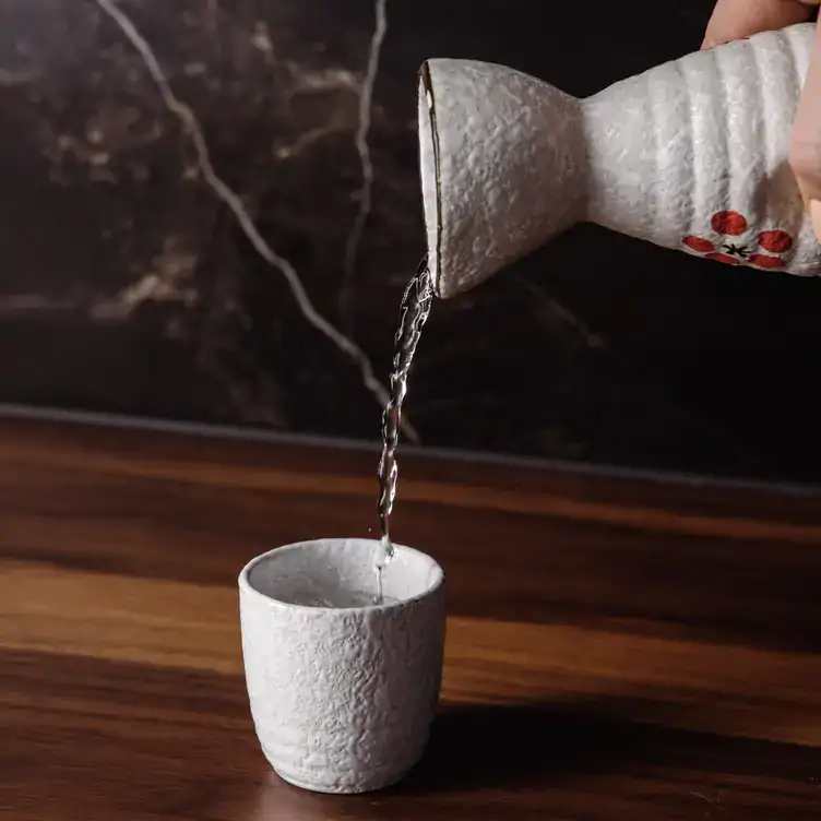 Someone pours a drink from a traditional sake bottle with a painting of a red flower at Koomo Restaurant and Bar, one of the best bars in Adelaide.