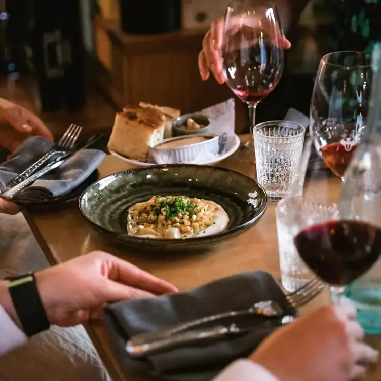 Diners reach out to wine glasses filled with red wine on a table with a creamy pasta dish at Good Gilbert, one of the best warm and cosy restaurants in Australia.