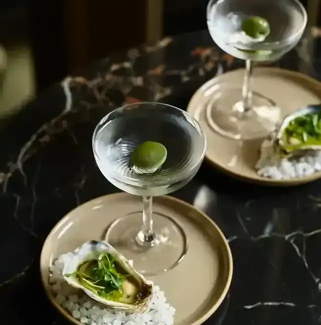 Two martinis with a green olive served alongside an oyster at Dean & Nancy on 22, one of the best cocktail bars in Sydney.