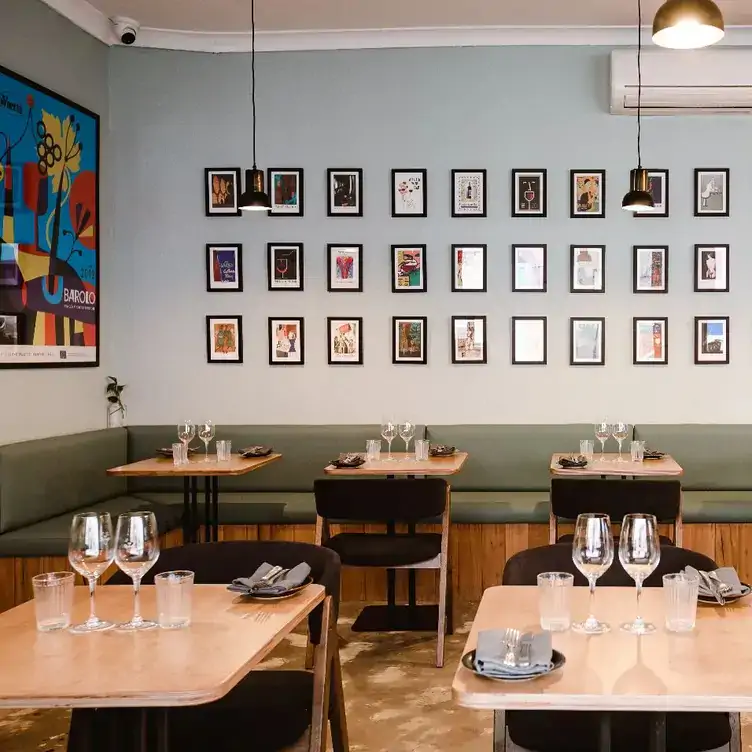 The interior of Good Gilbert, showing tables for two, bench seating and small prints lining the wall.