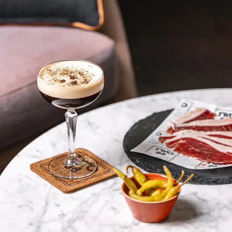 An espresso martini on a corkboard coaster served alongside a bowl of peppers and slices of cured meat at Two 88 Bar and Kitchen.