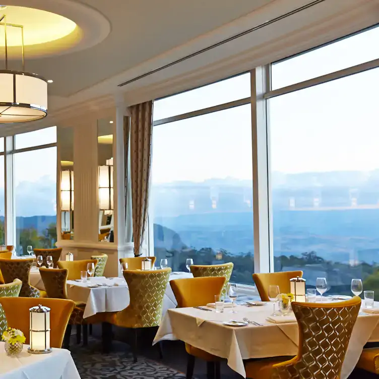 The interior of The Wintergarden at Hydro Majestic Blue Mountains, showing the gold-yellow plush chairs, large tables and forest views outside.