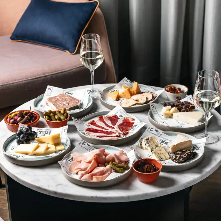 A table laid with multiple plates of cheese, cured meats and fruit alongside glasses of wine at Two 88 Bar and Kitchen, one of Sydney’s best cocktail bars.