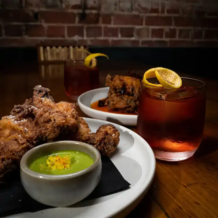 Plates of fried chicken served alongside cocktails garnished with lemon peel under the mood lighting at Udaberri Pintos Y Vino.