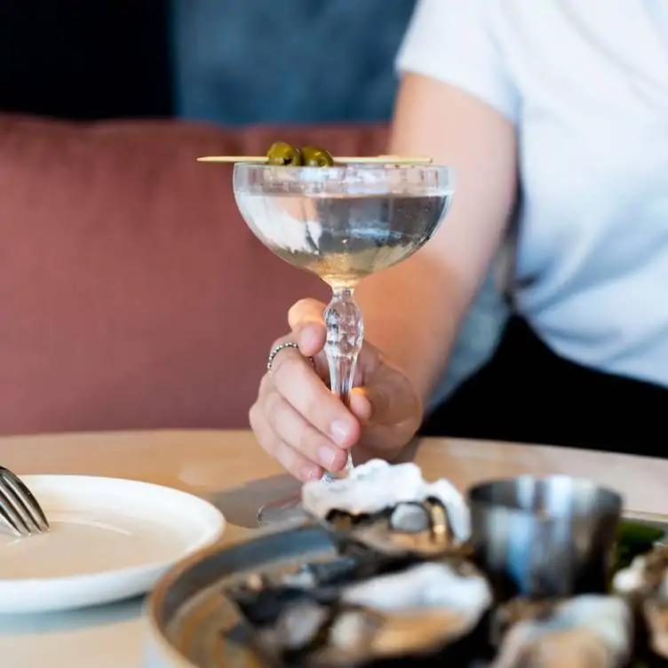 A diner holds a cocktail garnished with olives at The Loft Lounge and Bar, one of the best cocktail bars in Perth.