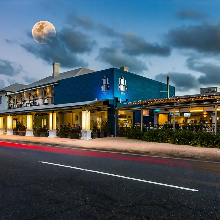 The exterior of the Full Moon Hotel, showing the blue walls, outdoor seating areas and an enhanced view of a full moon in the sky.