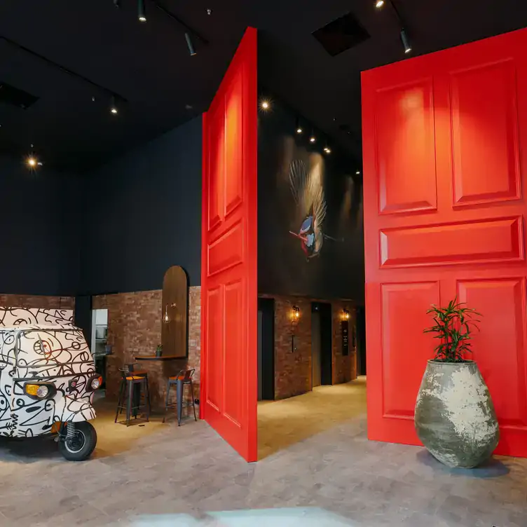 Two huge red doors in between a room with a drawn-on black and white vehicle and a room with a painting of a fairy wren on the wall at Izakaya Público