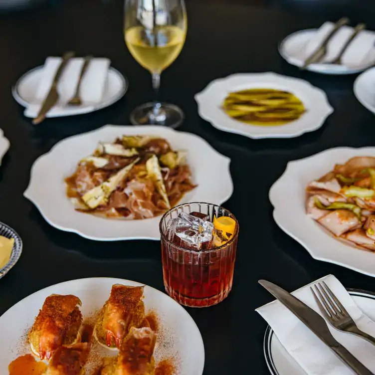 A table laid with multiple dishes, a glass of white wine and a garnished cocktail at Mummucc'.