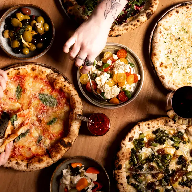 Diners reach across a table with different pizzas and salads at Yellow Matter Brewing, one of the best pubs in Adelaide.