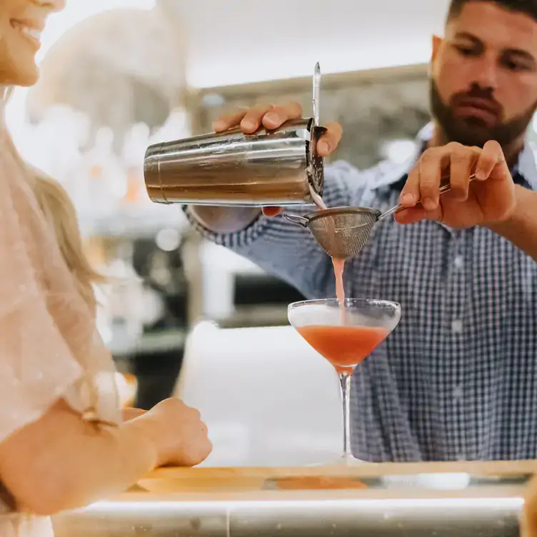 A bartender pours a pink cocktail through a small strainer and into a glass in front of a diner at Storehouse Subiaco.